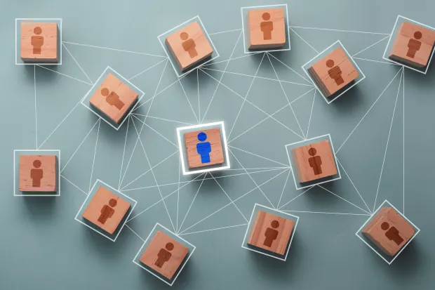 A network of wooden blocks with person icons connected by lines, centering around one blue figure. Illustrates centralized identity management with one central identity controlling access across multiple nodes.