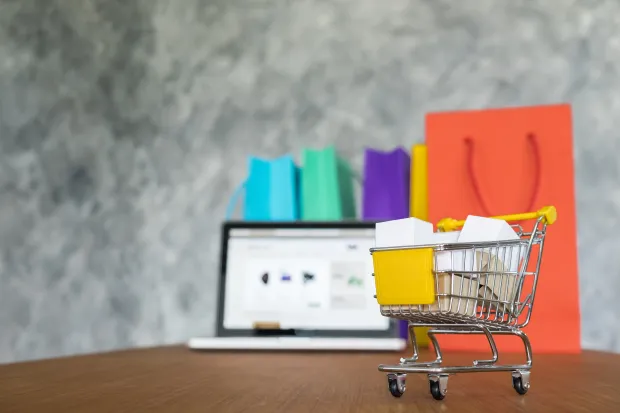 A shopping cart placed on a table with laptop.