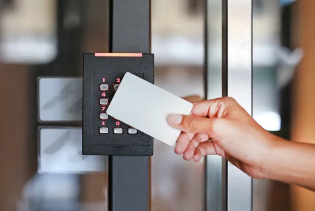 A person holds an access card near a keypad security system. Represents physical access control, often used as a metaphor for digital access control systems.