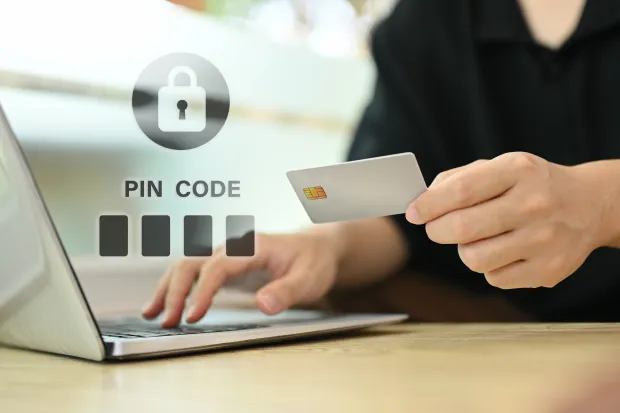 A person enters a PIN code on a laptop while holding a credit card, symbolizing secure online authentication. Illustrates digital payment security and multi-factor authentication.